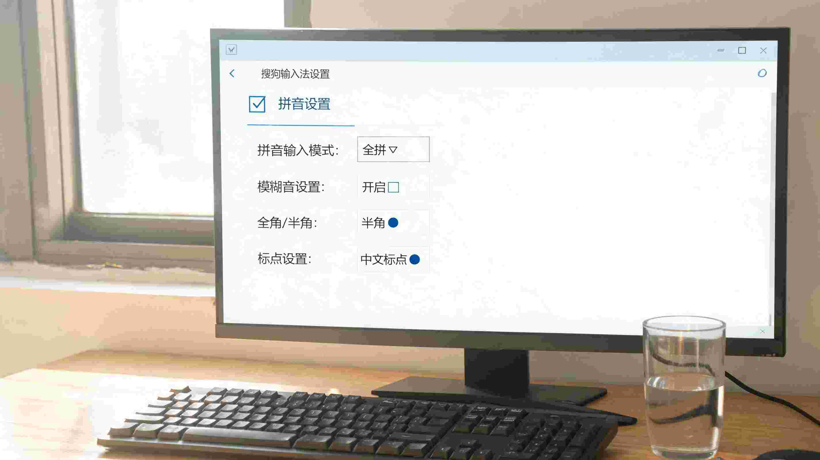 书桌上的键盘，屏幕显示搜狗输入法如何切换拼音设置界面，桌角放着水杯，自然光
